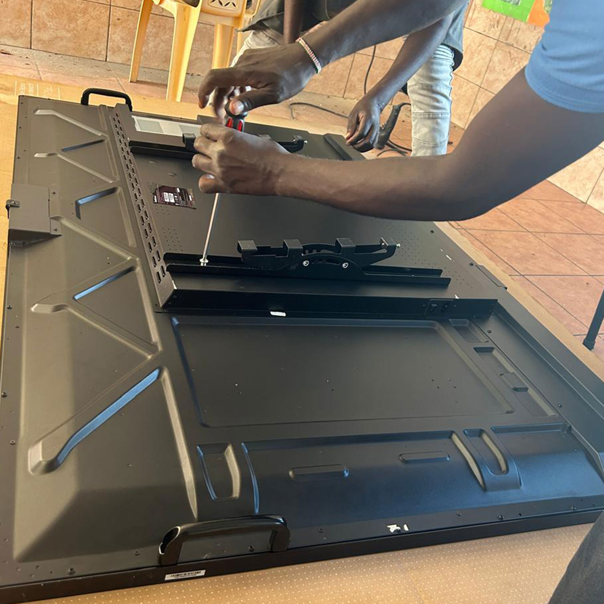 Person's hands using a screwdriver to open a large flat-screen television laid on its back on a workshop floor.